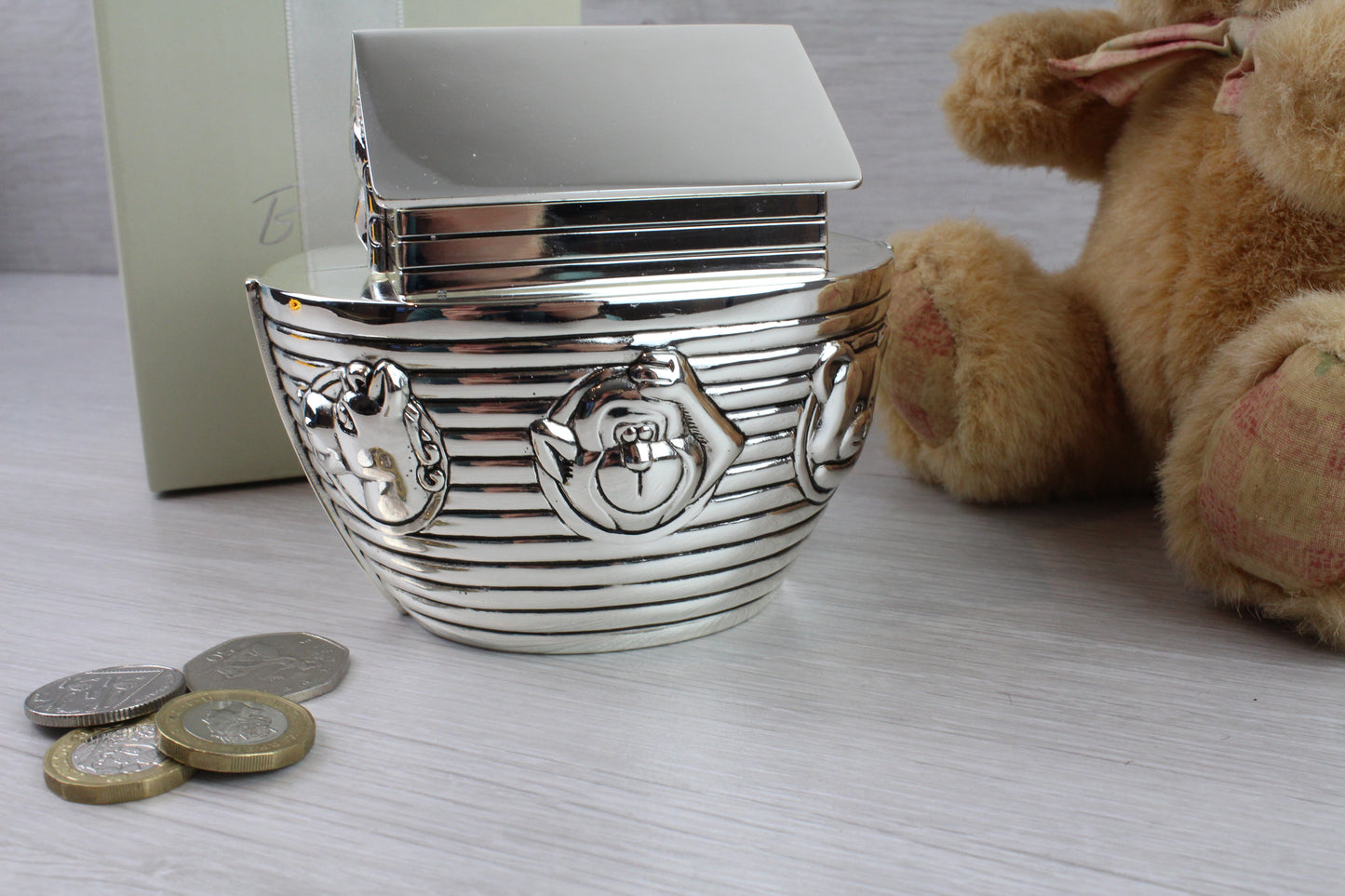 Showing the left side of Noah's Ark Money Box with some animals designs and coins as a prop.