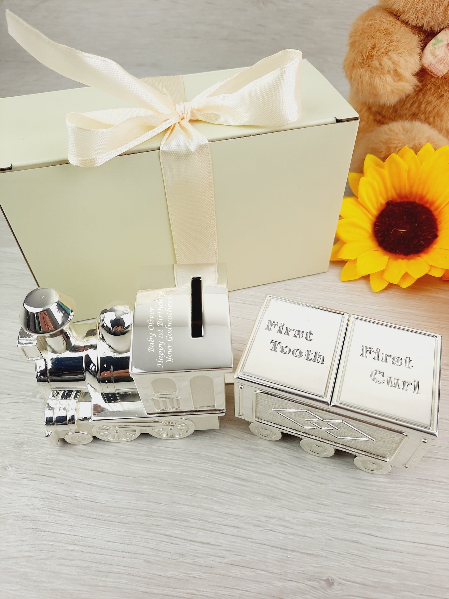 Personalised Engraved Money Box with Baby Tooth and Curl Train. There's cream gift box with peach ribbon and a sunflower as props.