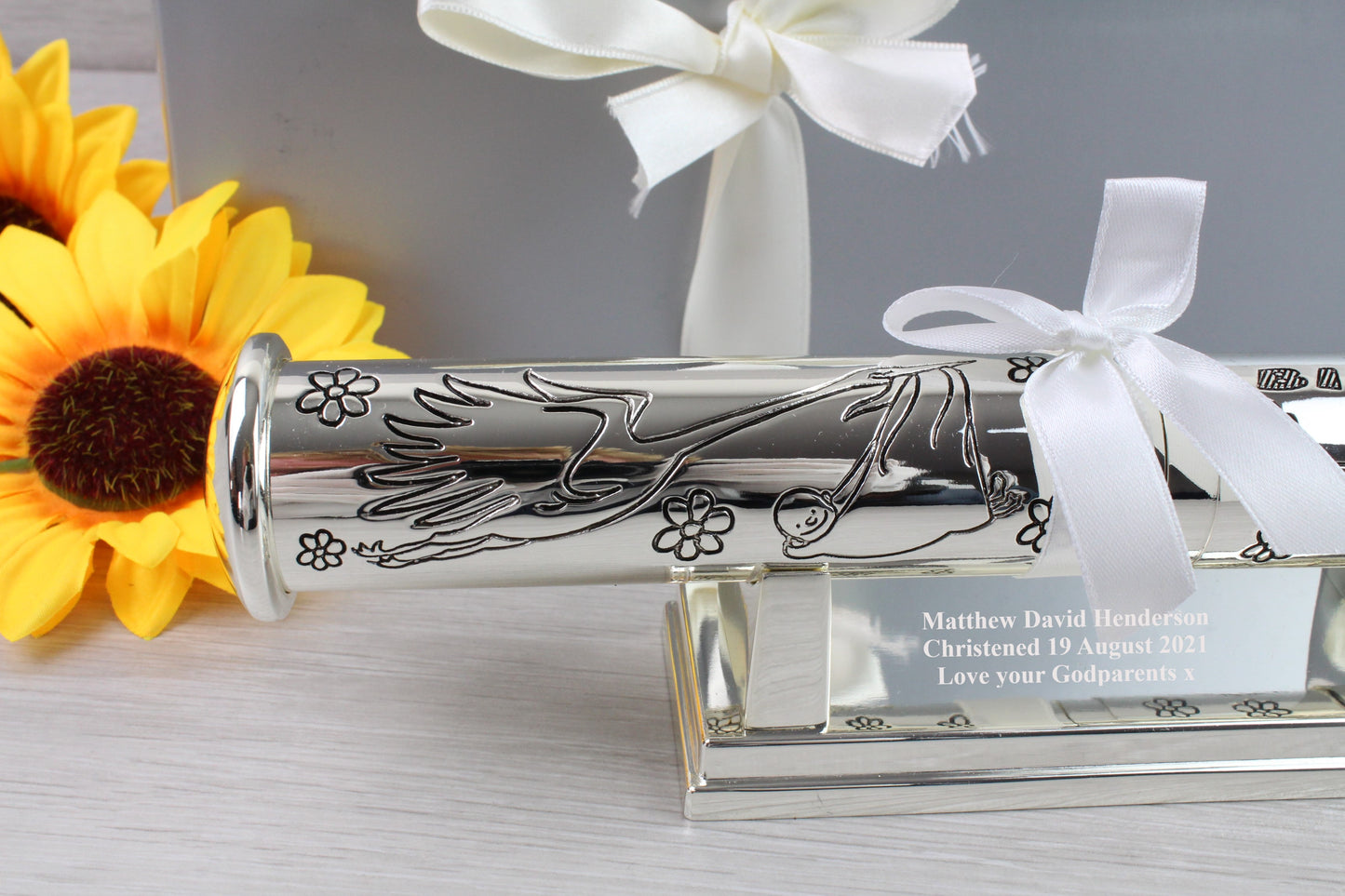 The other side of birth certificate holder with flowers and birds engraved with white ribbon and sunflowers as props. There's also a personalised message on the stand below that says "Matthew David Henderson Christened 19 August 2021 Love your Godparents x"
