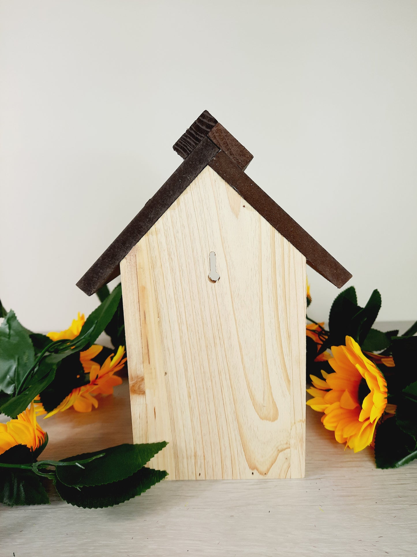 Back side of the bird nesting box with faux sunflower surrounding it as props.
