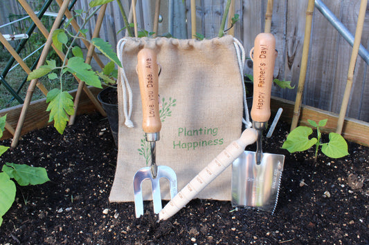 Personalised fork that says "Love you Dada, Ava", dibber with measurements, personalised trowel that says "Happy Father's Day!" and there's a jute bag with wordings "Planting Happiness"