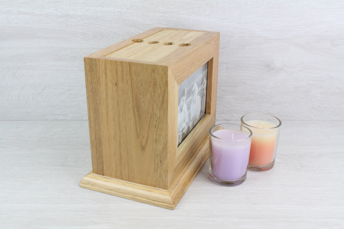 Sideview of a Personalised Oak Wooden Photo Frame and Album Holder. Inside the wooden photo frame, there's a black and white family photo with two young girls and their parents. Also, beside the wooden frame, there are two not lighted candles (colour purple and orange).