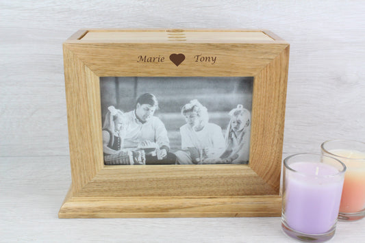 Personalised Oak Wooden Photo Frame and Album Holder with names and a heart design that says "Marie <3 Tony" Inside the wooden photo frame, there's a black and white family photo with two young girls and their parents. Also, beside the wooden frame, there are two not lighted candles (colour purple and orange).