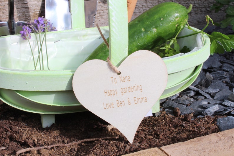 Engraved wood heart that says "To Nana Happy gardening Love Ben & Emma" tied on with jute string.