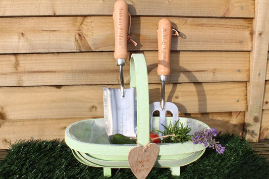 Trowel, fork and vegetables placed on the softwood trug with engraved wood heart tied on with jute string.