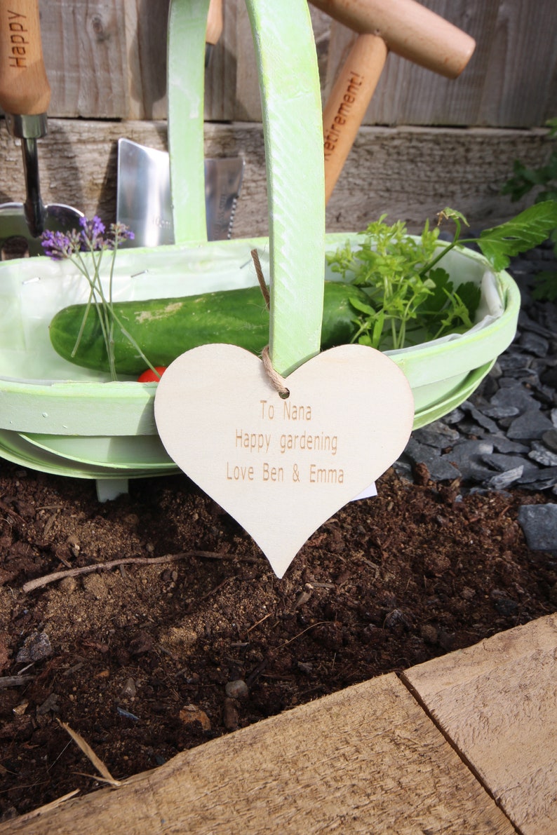 Engraved wood heart that says "To Nana Happy gardening Love Ben & Emma" tied on with jute string.